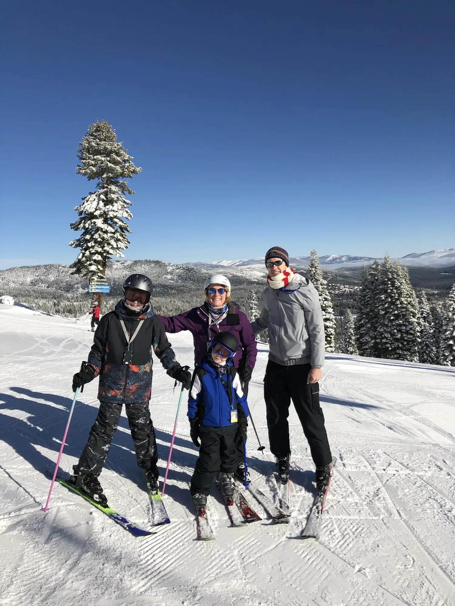 A family of four on skis at the top of a groomed run on a bluebird day